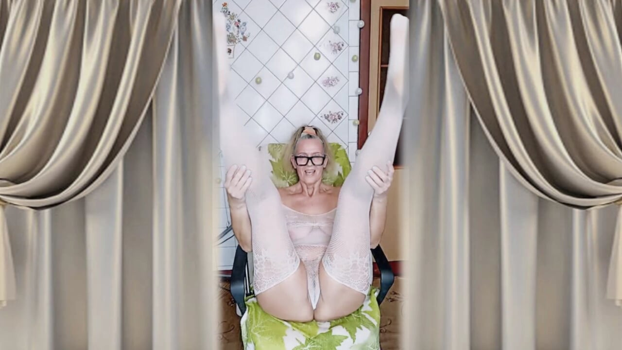 Cheerful housewife Lukerya flirts in an open, transparent white jumpsuit in the kitchen.
