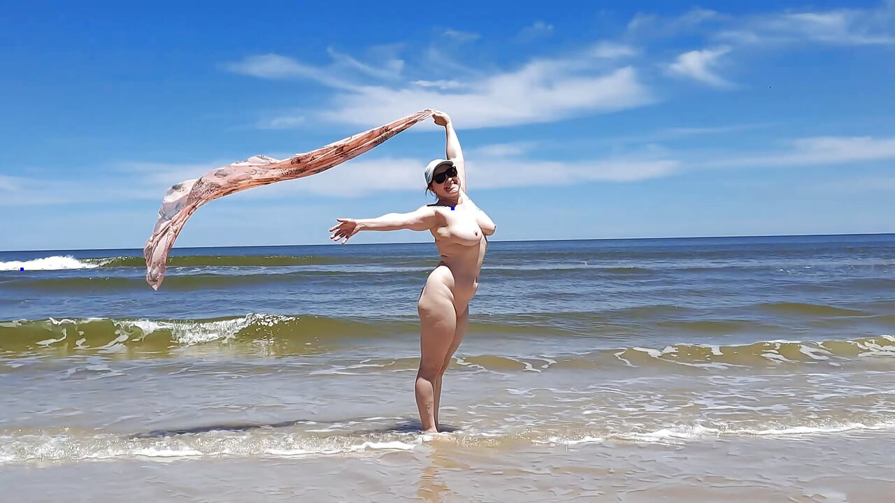 Amatorskie filmowanie. Nudysta bawi się falami na brzegu oceanu.