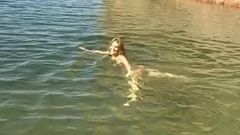 Cute young brunette strips by the water and goes skinny dipping