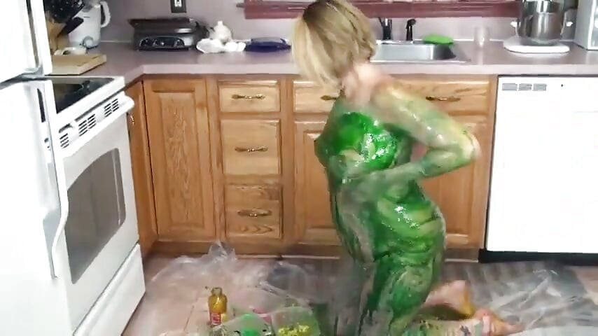 Loira na cozinha esfrega tinta verde sobre seus peitos e bunda