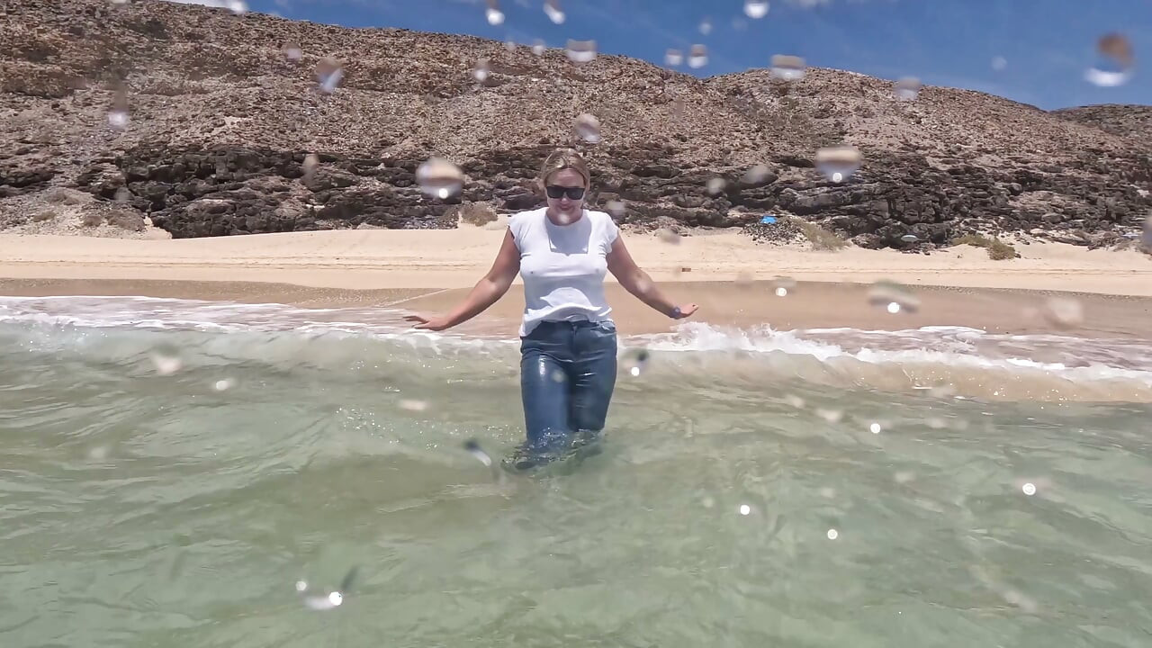Menina molhando jeans no oceano e nadando em camiseta branca molhada