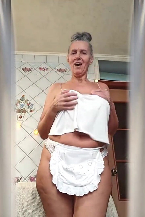 Quente dona de casa Lukeria flerta na cozinha em uma tanga branca e um pequeno avental