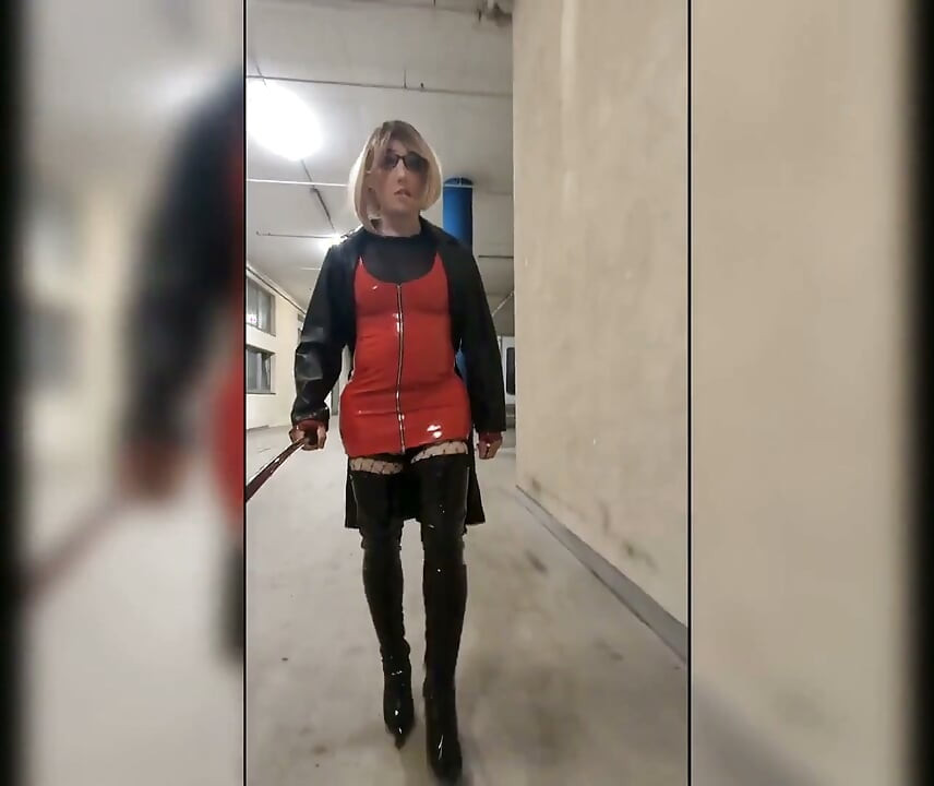 Spaceruj po parkingu, blondynka w overknee boots, czerwona sukienka PCV i długi skórzany płaszcz