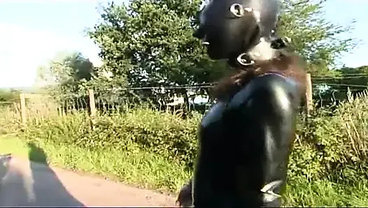 Lateksli fetiş köle yürüyor ve çimlerde dildo emiyor