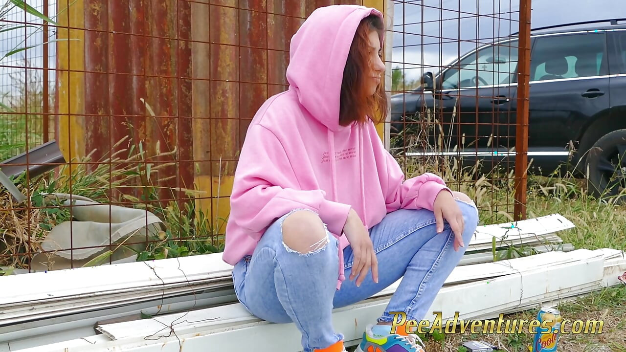Hipster girl with a hoodie pee trough her jeans and pee next to the wheel of the car