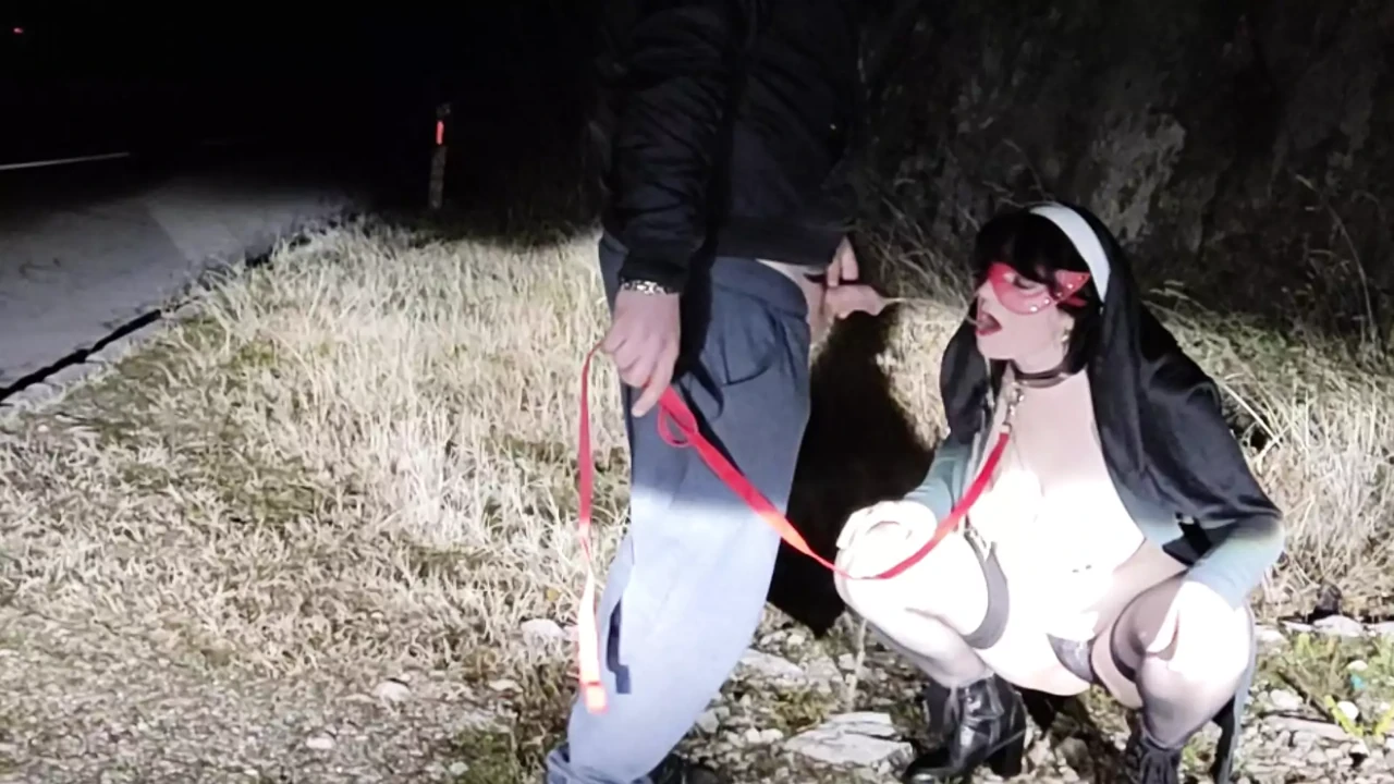 Piss Slut Wife in a Nun costume with a dog collar around her neck receives a golden shower her mouth from the side of the road