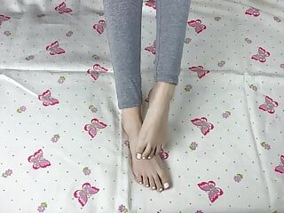 Uma garota de legging cinza com pernas longas acaricia os pés com uma pedicure branca