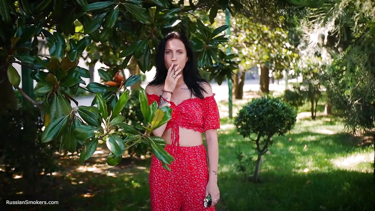Sensual morena en vestido rojo fumando cigarrillo enrollado
