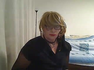 Une trans MILF excitée s'exhibe et se doigte devant une webcam dans une résille noire, une robe courte et des talons hauts