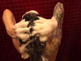 Дівчина миє волосся шампунем із великою кількістю піни під душем