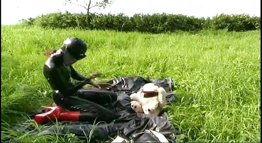 Esclavo fetiche en látex camina y chupa un consolador en la hierba