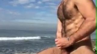 Super hete harige man trekt zich af op het strand