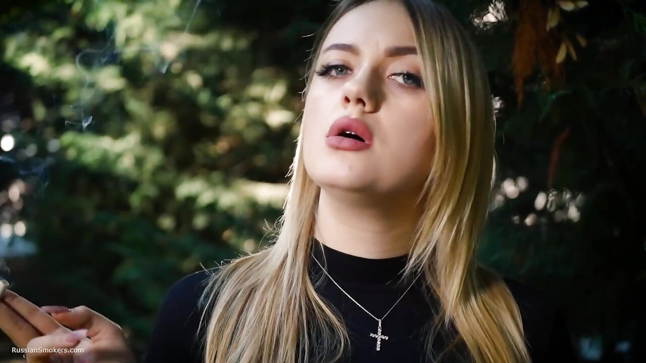 Hete blonde babe die in de natuur een zwarte sigaret rookt