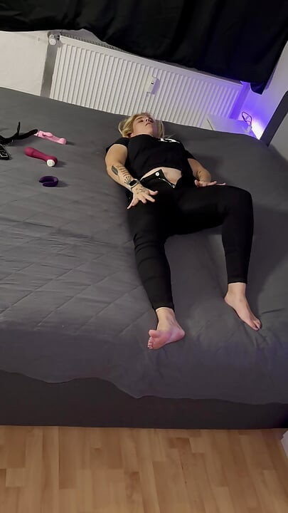 Blonde lady in black gets orgasms while standing behind the camera and watching her