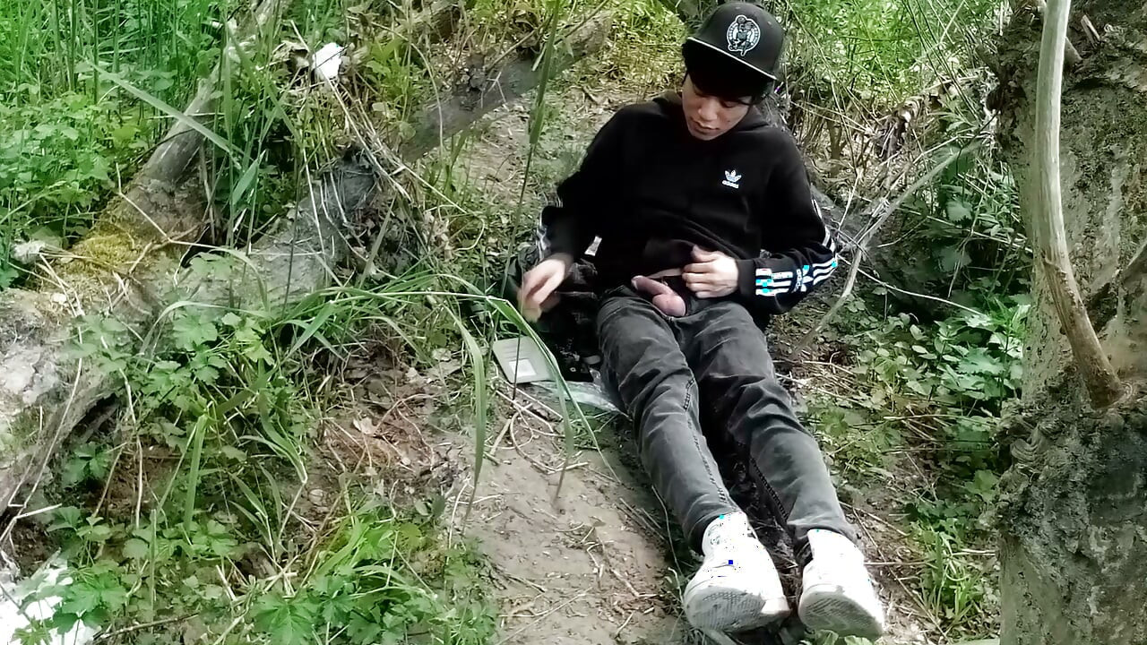 The cute gay twink jerking off his cock, pulled through his fly while outdoors, is Jon Arteen
