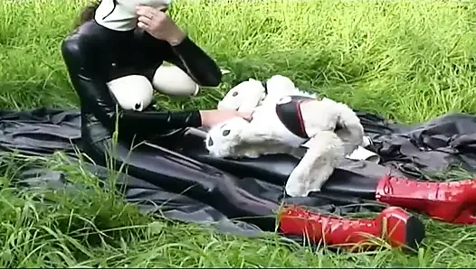 Fetish slave in latex walks and sucks a dildo on the grass