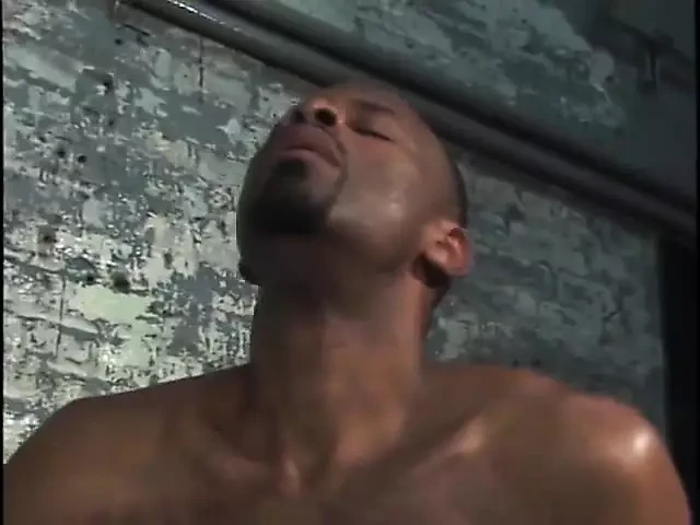 Two horny black men suck dick by a cement wall.