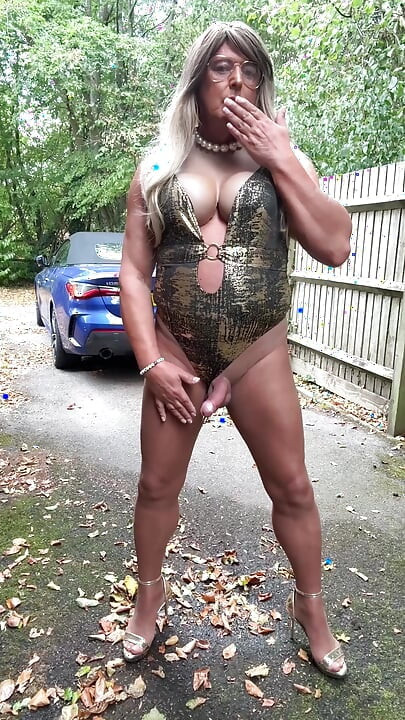 Seksi transvestit kellycd2022 u zlatnom kupaćem kostimu i štiklama čisti lišće