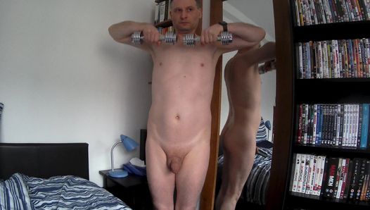 Kudoslong totalement nu devant un miroir, sa bite est petite et flasque pendant qu'il fait de l'exercice avec des poids