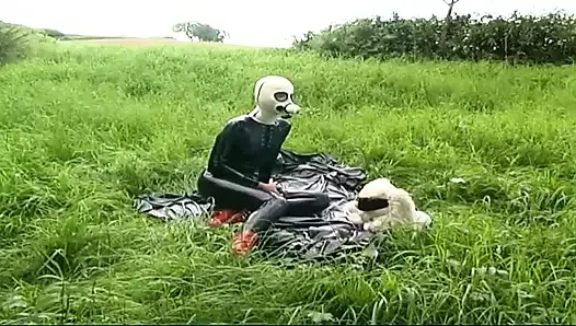 Fetish slave in latex walks and sucks a dildo on the grass