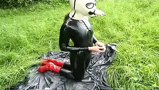 Lateksli fetiş köle yürüyor ve çimlerde dildo emiyor