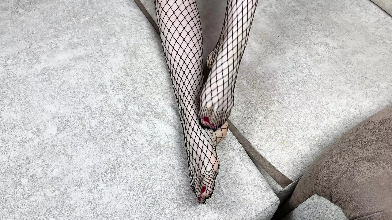 Mistress in black fishnet stockings caresses her legs with pedicure