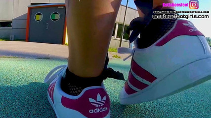 Menina de superstars da adidas vermelha brinca com os sapatos, mergulhando meias arrastão