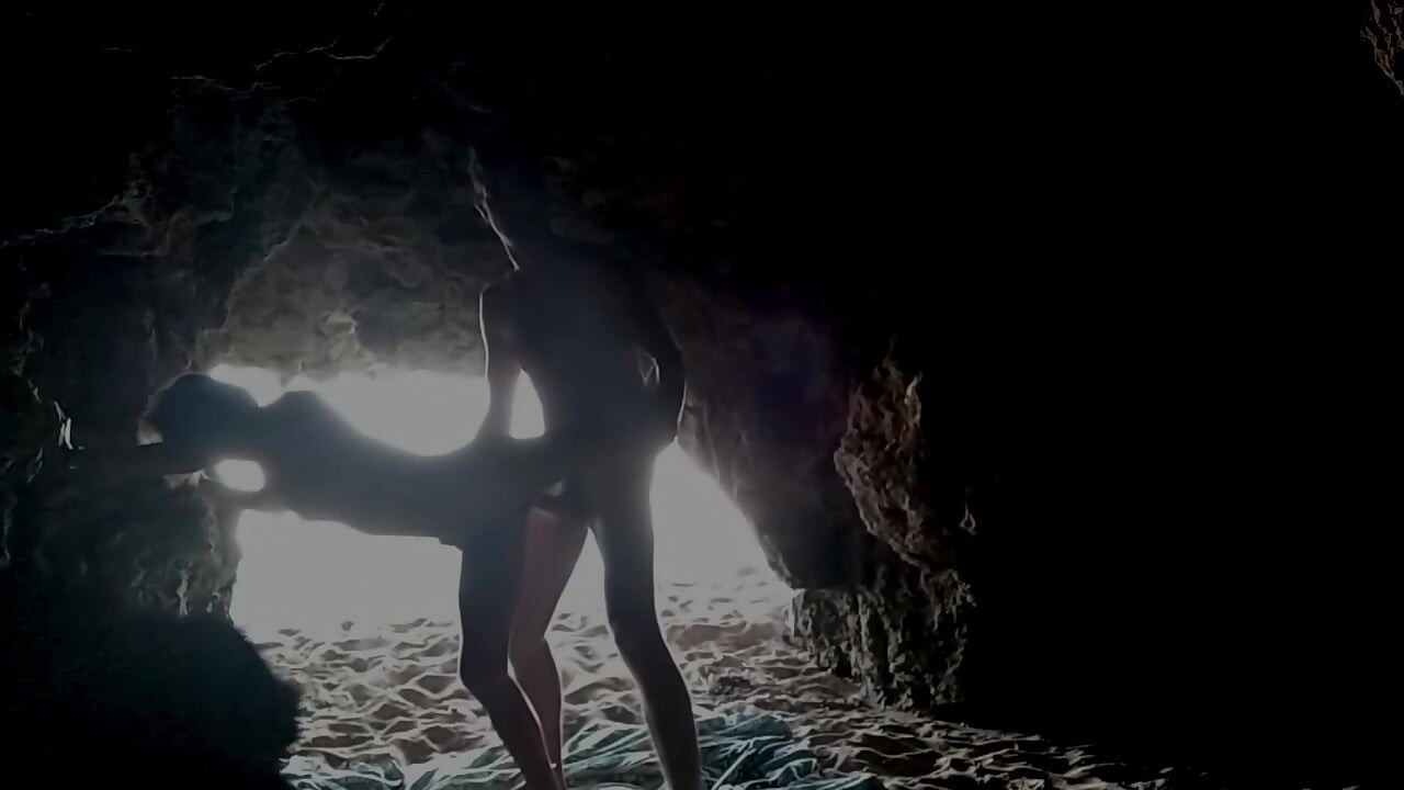 Casal gravado na praia, dentro da caverna