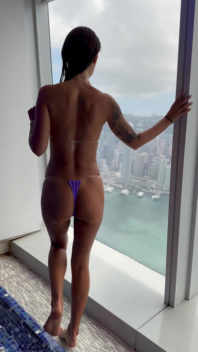 Monika Fox in Purple Bikini Swims in Pool & Poses by Window Against Background of City