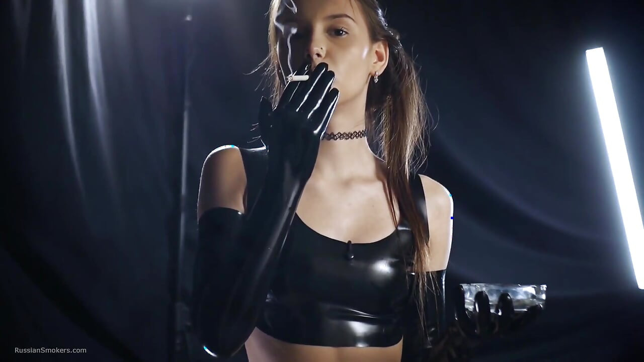 Une brune fume dans une tenue noire en latex, scène sensuelle lente