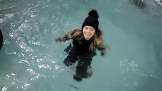 Une fille wetlook avec des vêtements d&#39;hiver nage dans la piscine