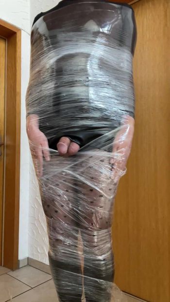 Travestiet gekleed in pantyleerlaarzen en rok strak gewikkeld in plastic wikkel mummification zelfbondage