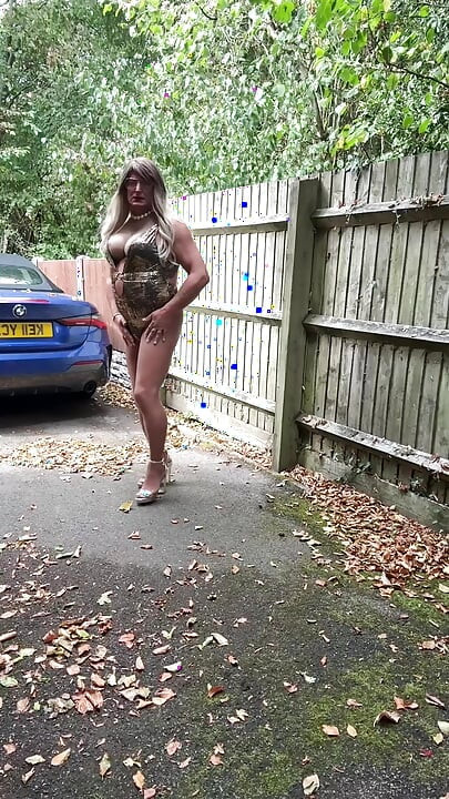 Seksi transvestit kellycd2022 u zlatnom kupaćem kostimu i štiklama čisti lišće