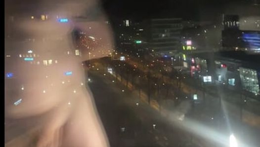 de pie desnudo frente a la ventana del hotel a lo largo de una calle concurrida