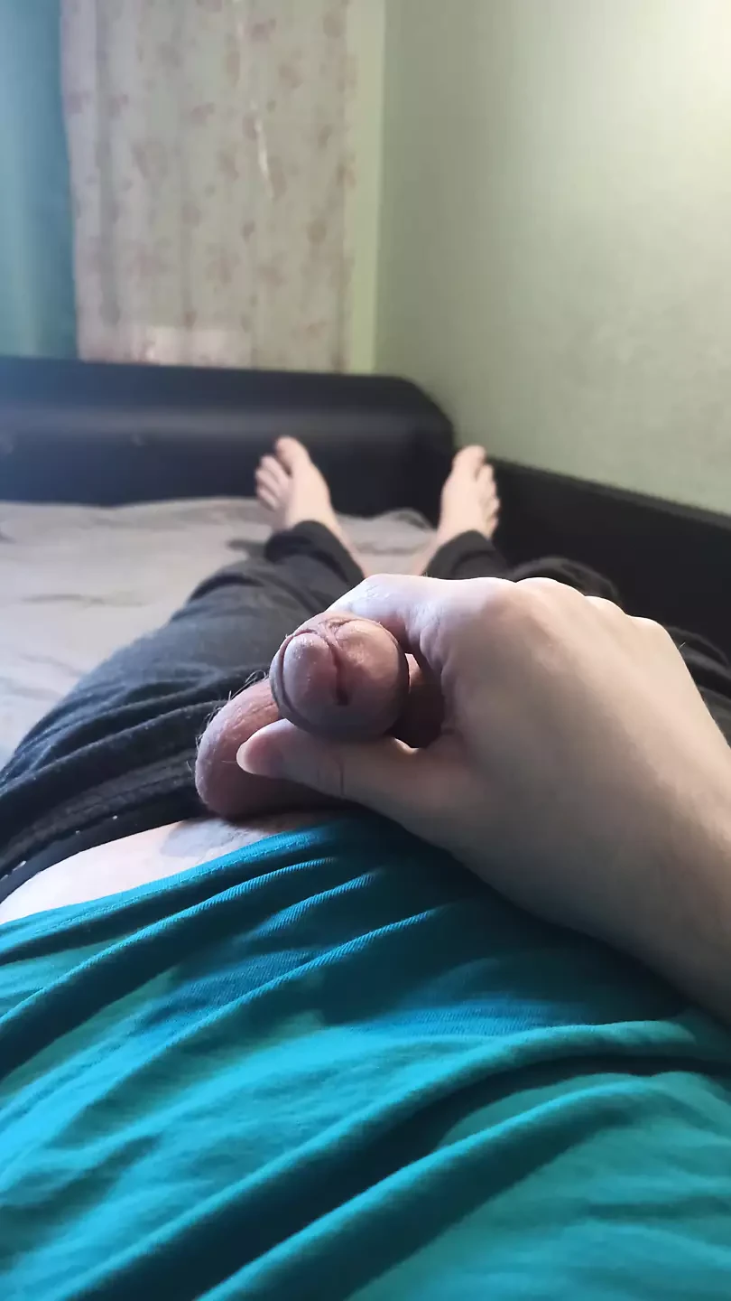 Un tip în tricou albastru își masturbează pula întinsă pe pat