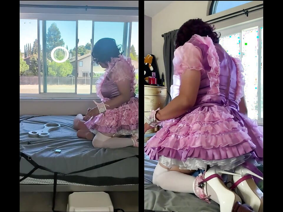 ピンクのサテンのシシーメイドがロックされたままセックスドールのおもちゃに乗っている