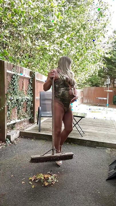 Seksi transvestit kellycd2022 u zlatnom kupaćem kostimu i štiklama čisti lišće