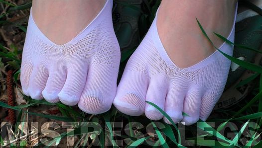 Diosa pies en lindos calcetines blancos con jeans en el campo de hierba de primavera