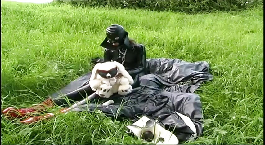 Fetish slave in latex walks and sucks a dildo on the grass