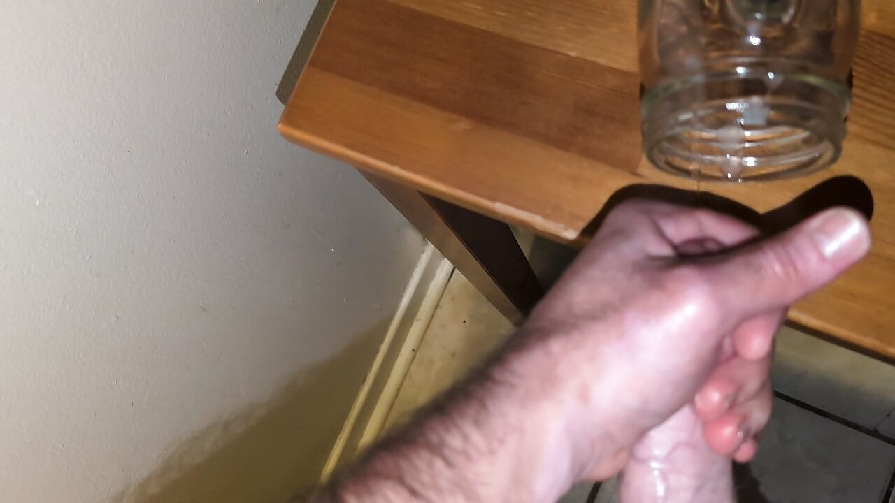 Un bărbat gras își masturbează pula tare și ejaculează într-un pahar