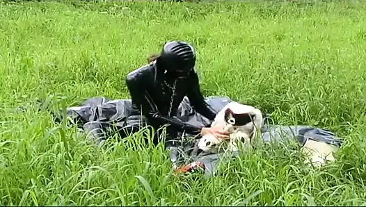 Fetisch-sklavin in latex geht und lutscht einen dildo auf dem gras