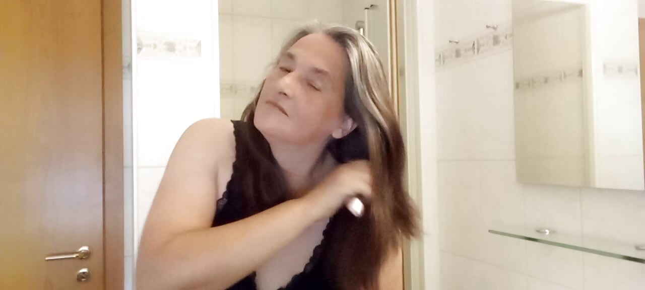 Mulher madura com fios prateados reais penteia lentamente o seu cabelo comprido