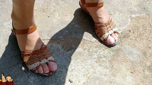 Nackte Ehefrau mit Sandalen, die ihre Füße vor dem Garten blankziehen