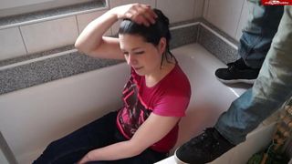 A girl in clothes sits in the bathroom and receives a stream