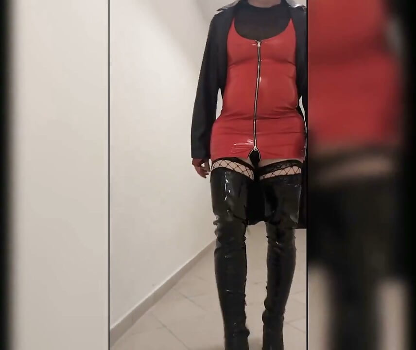 Caminhada na casa de estacionamento, loira em botas overknee, vestido vermelho de pvc e casaco de couro longo