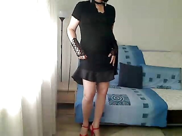 horny MILF tranny shows off her body in a black satin dress, bare slender legs, thong and red heels