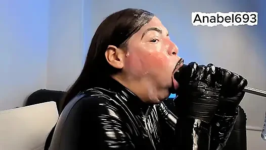 Lateks, lateks eldivenler, lateks takım elbise ve siyah dudaklarla giyinmiş bir iblis, şehvetli bir şekilde yarağını emiyor ve tükürüyor