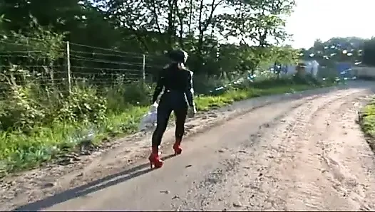 Fetish slave in latex walks and sucks a dildo on the grass
