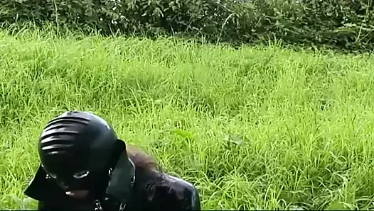 Lateksli fetiş köle yürüyor ve çimlerde dildo emiyor