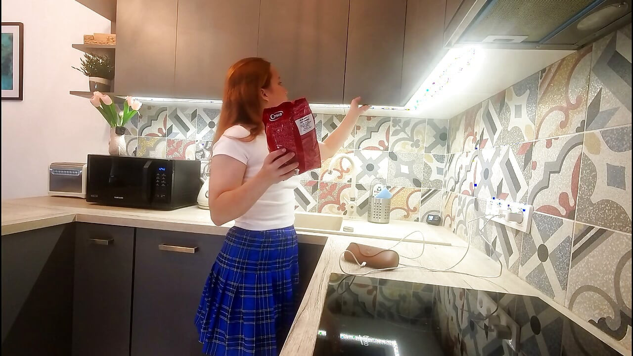 Petite vraie étudiante sexy en mini-jupe d'uniforme scolaire écossais qui montre ses jambes et ses culottes en coton dans la cuisine